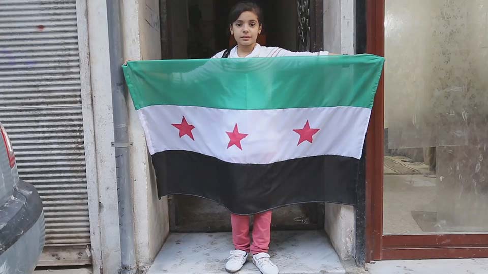 A young girl holds the flag of the Syrian National Coalition