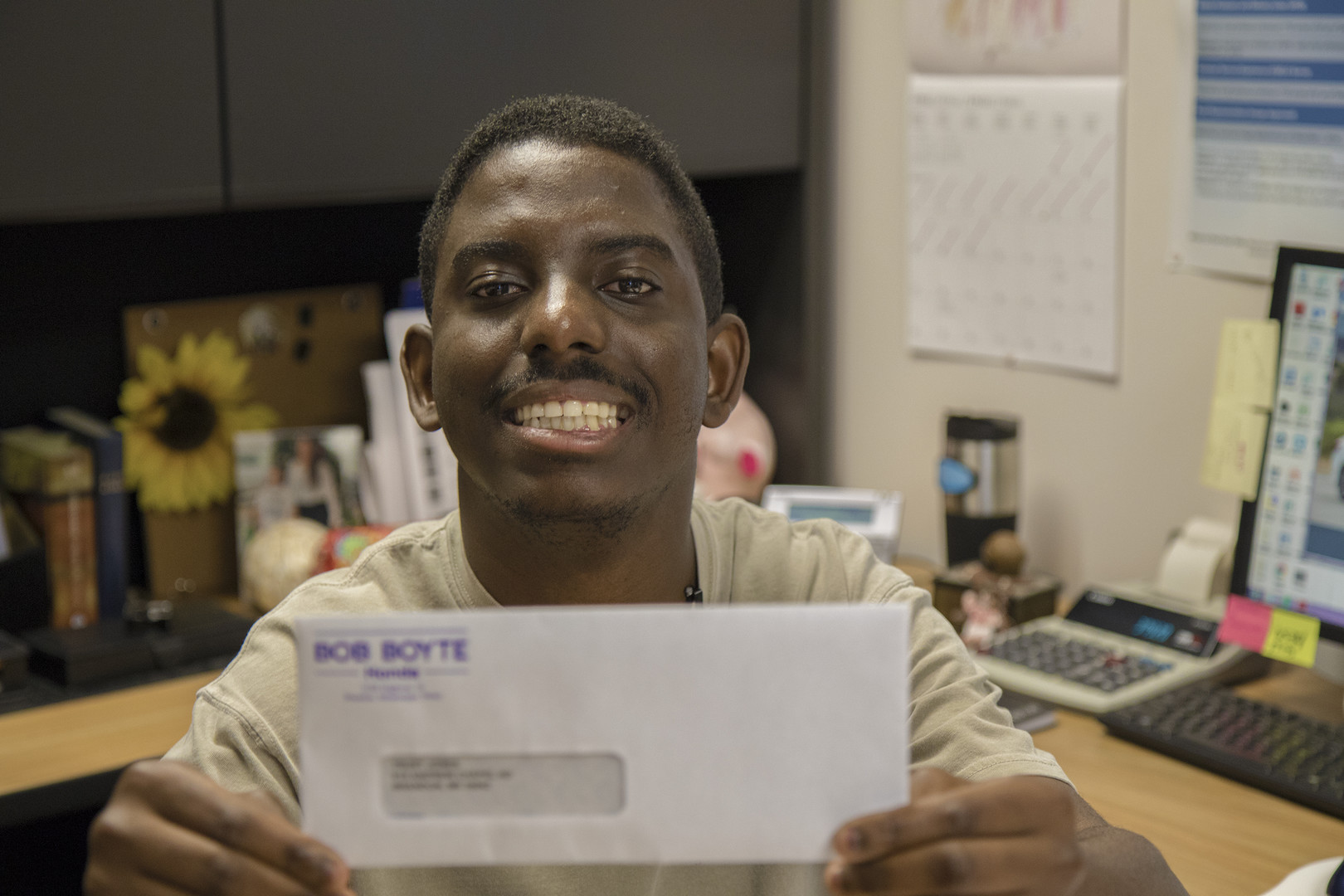 A man smiles as he holds an envelope up to the camera.