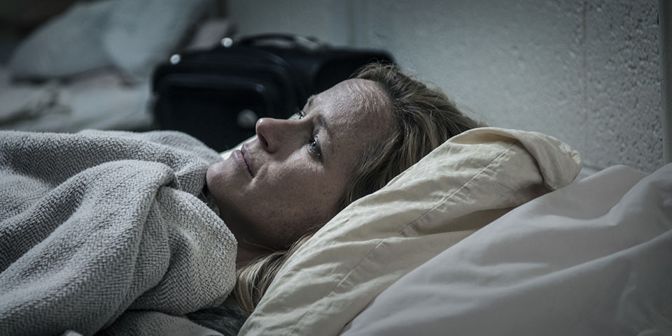 A woman lays in an institutional bed.