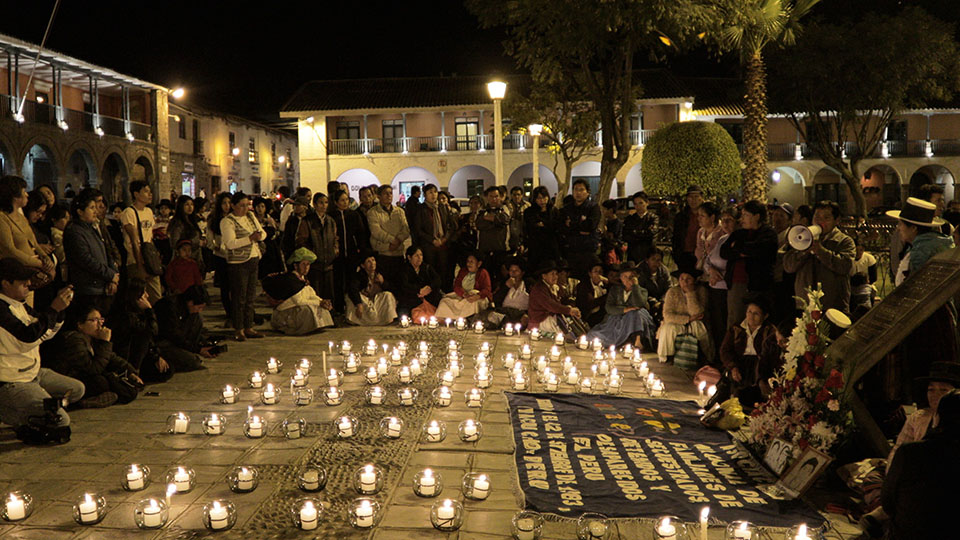 A crowd of people gathers around an area of illuminated remembrance candles.