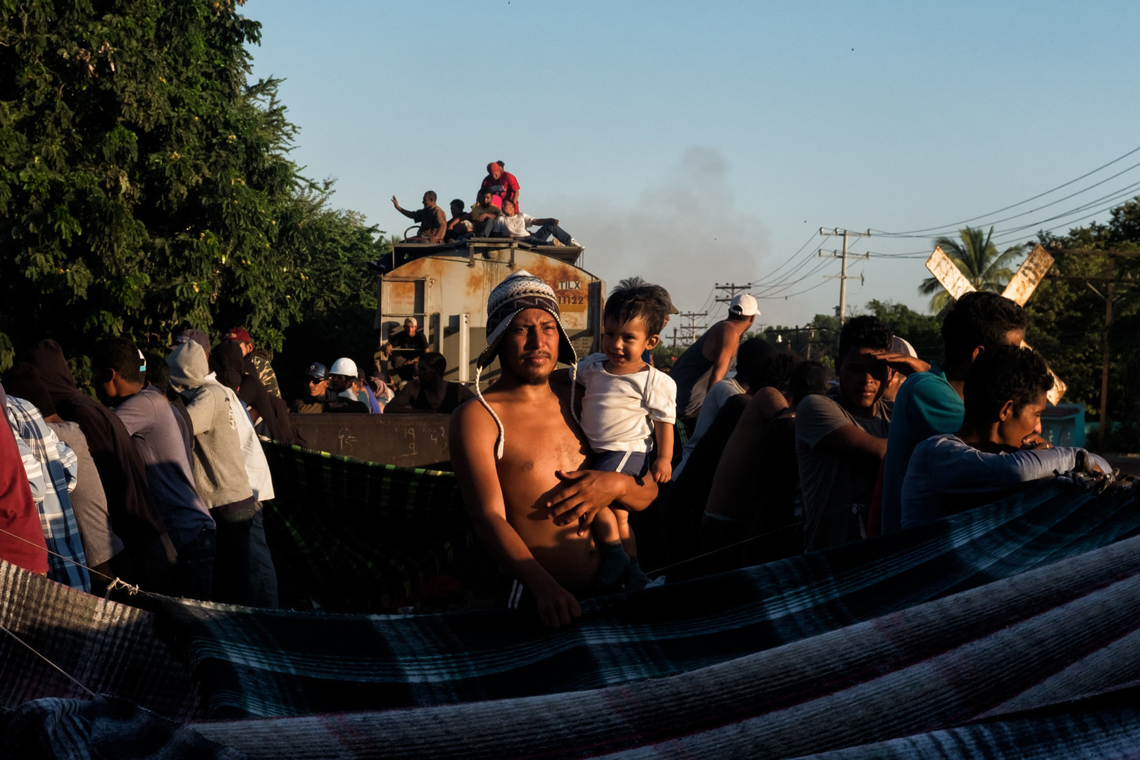 A man holds a small boy amongst others in a crowd on a flatbed train car.